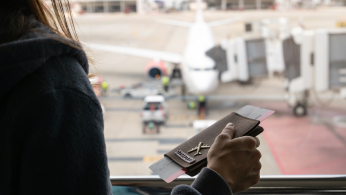 Young Woman Traveler With Luggage Holding Passport Looking At The Airplan